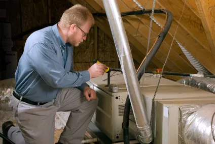 HVAC technician using a tool to work on an HVAC system in an attic.